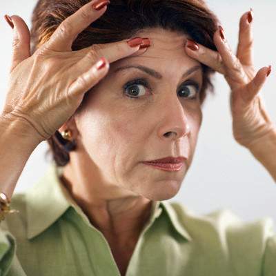 A woman looking at her forehead wrinkles