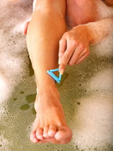 Lady shaving her legs in a bathtub